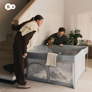 Familia con bebé usando el corral de juegos Kinderkraft ZIKI grey en casa, con lateral de cremallera, malla transpirable y suelo blando