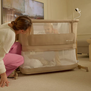 Madre mirando a su hijo en la cuna 3 en 1 NESTE GROW 2 de Kinderkraft beige, con colchón en posición más baja.