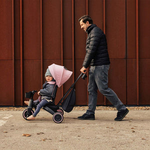 Padre paseando a un niño en el triciclo Kinderkraft JAZZ 3 beige con mango telescópico ajustable, capota UPF50+ y asiento reversible.