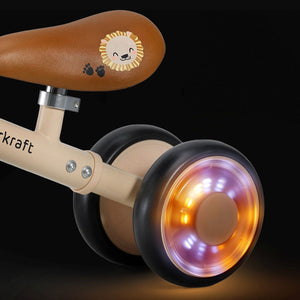 Triciclo correpasillos Kinderkraft CUTIE FLASH beige con ruedas con rodamiento ABEC-7 y luces LED RGB, sillín acolchado ajustable. Andador con estructura de acero estable. Vista detalle ruedas trasera con luces.