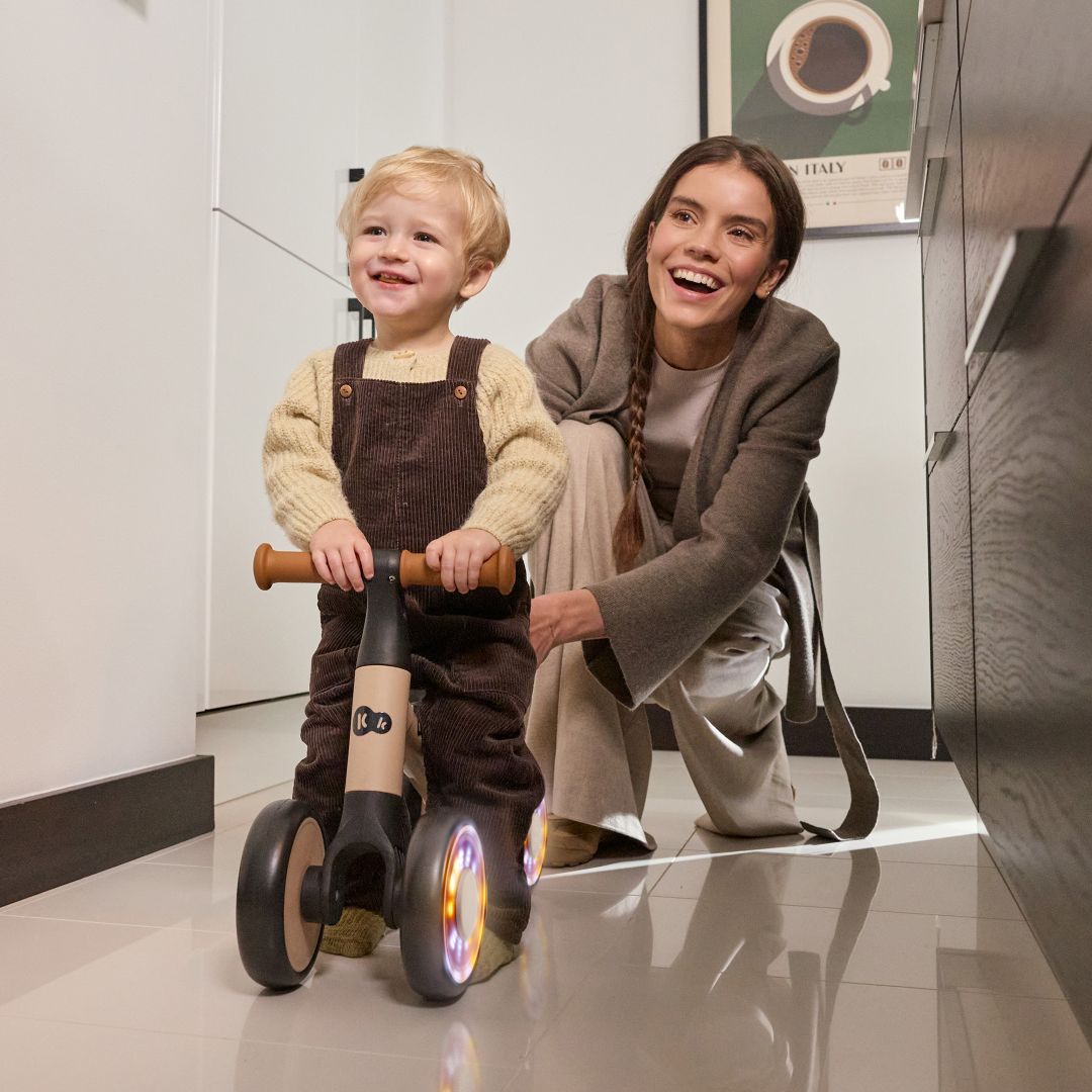 Madre con niño usando el triciclo correpasillos Kinderkraft CUTIE FLASH beige con ruedas con rodamiento ABEC-7 y luces LED RGB.