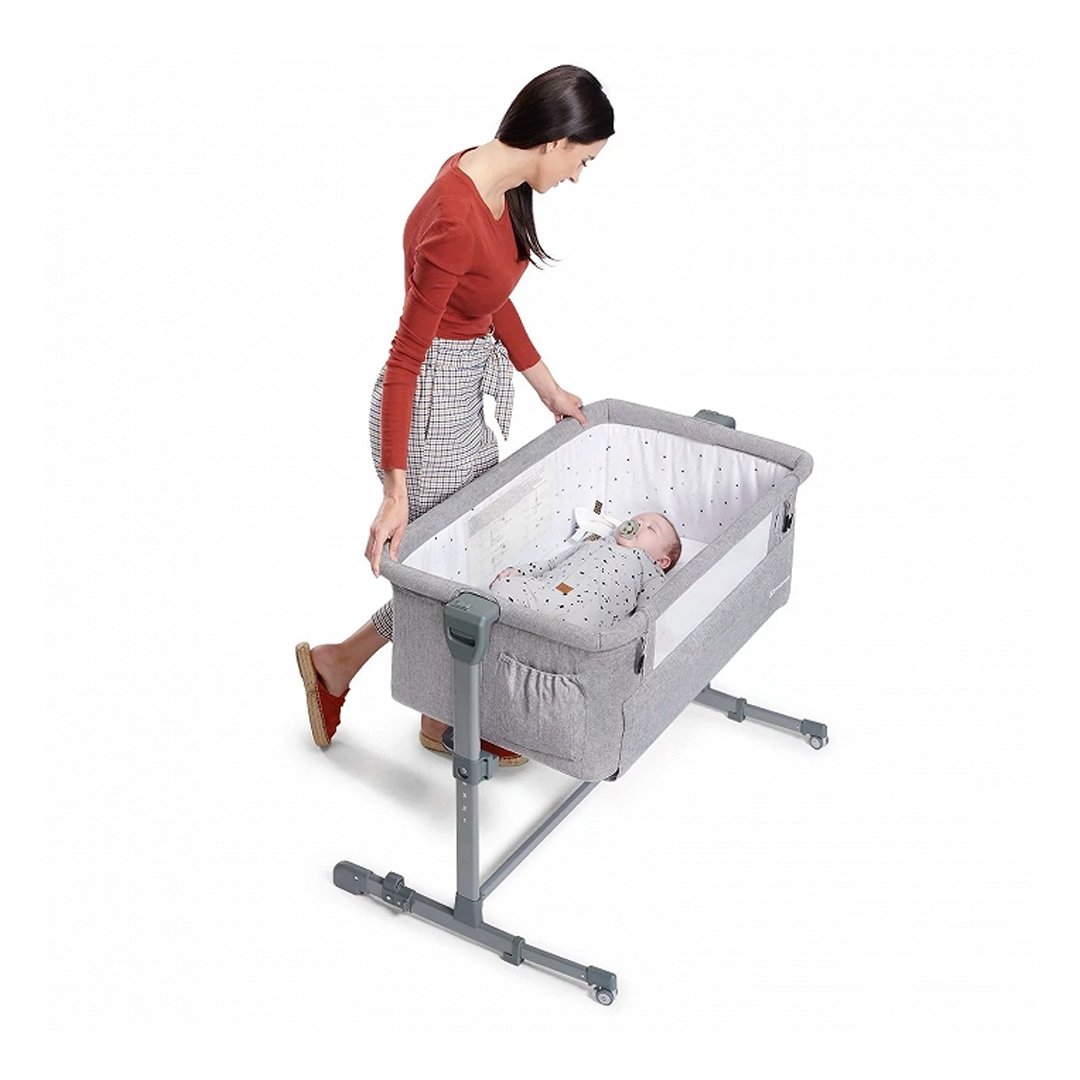 Mamá revisando a su bebé en cuna colecho Kinderkraft NESTE UP gris claro, estructura con ruedas y altura ajustable, colchón incluido