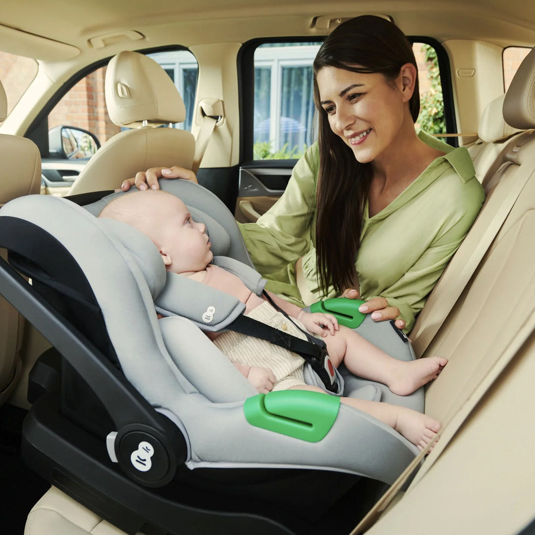 Mamá abrochando el arnés de su bebé recién nacido en la silla nido Kinderkraft MINK PRO i-Size instalada contramarcha en asiento trasero del auto